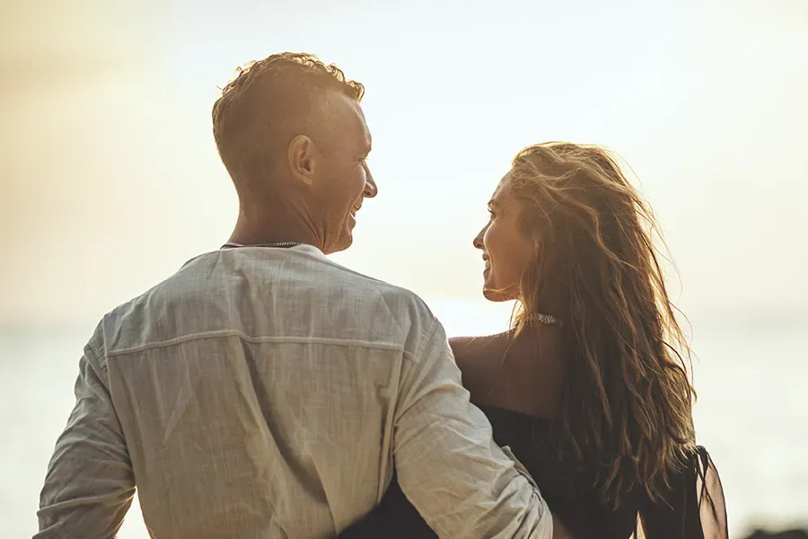 A couple gazes at each other on the beach at sunrise, viewed from behind. Schedule Anti-Aging treatment from ProCare Wellness Institute in Virginia Beach.
