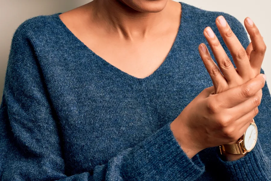 Close up of a woman in a blue sweater massaging one aching hand with the other. Get help for arthritis from ProCare Wellness Institute in Virginia Beach.