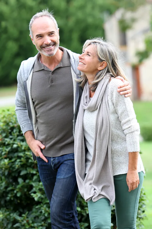 A mature couple in gray toned clothes and jeans walk happily outside, happy with their successful bioidentical hormone treatments from ProCare Wellness Institute in Virginia Beach.