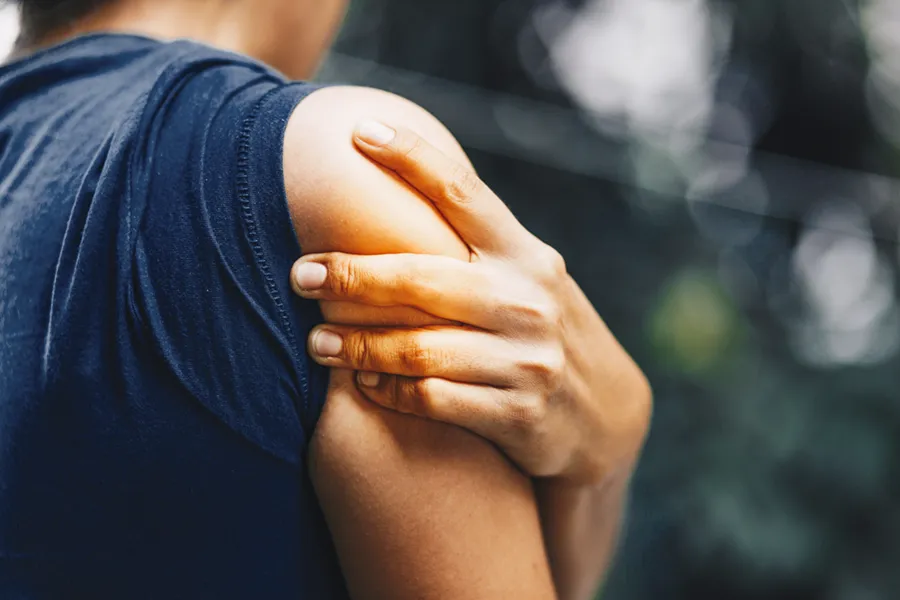 A woman holds her shoulder in pain. schedule treatment for bursitis from ProCare Wellness Institute in Virginia Beach.