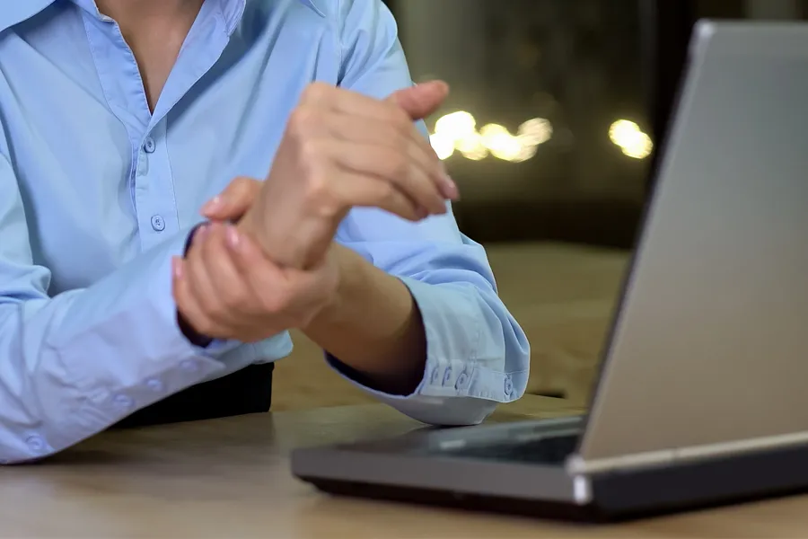 A woman sits in front of her computer rubbing her hand in pain. Schedule treatment for carpal tunnel syndrome from ProCare Wellness Institute in Virginia Beach.