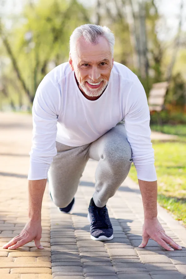 Degenerative-Disc-Disease-Treatment A senior man with grey hair, actively performing a starting block position on a paved path in a park excited to maintain vitality and an active lifestyle because of ProCare Wellness Institute's Degenerative Disc Disease Treatments in Virginia Beach.