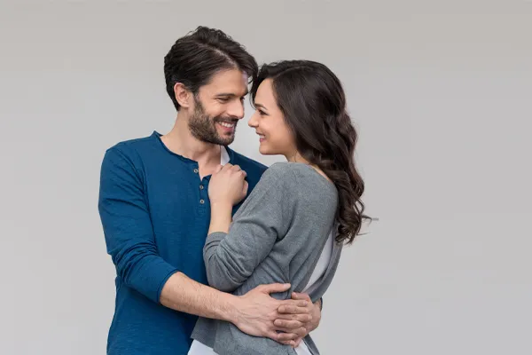 A man in a blue shirt embracing a woman in a gray shirt smiles due to his successful erectile dysfunction care from ProCare Wellness Institute in Virginia Beach.