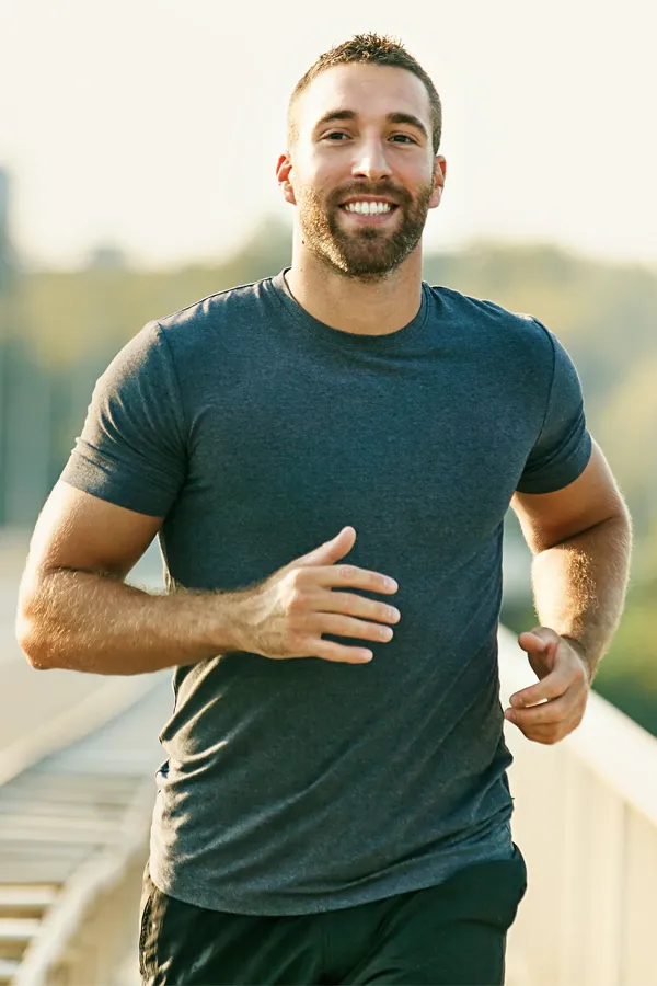 A fit, young man jogging in an urban setting during golden hour. He has a warm smile and looks energized and healthy while maintaining an active lifestyle after receiving Hyaluronic Acid Injections for Joint Pain by ProCare Wellness Institute in Virginia Beach.