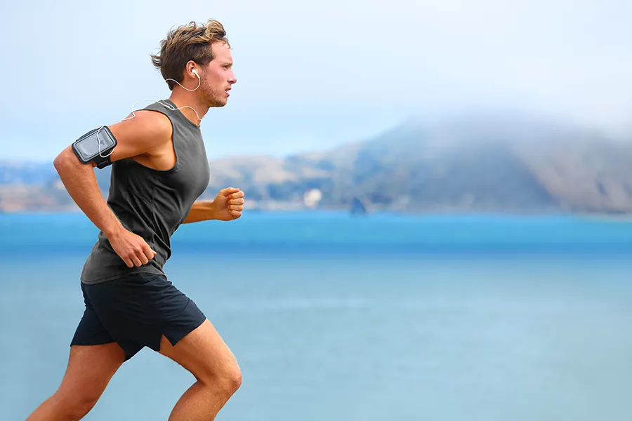 A focused young man running pain-free along a coastal path with a scenic view of the sea after receiving Hyaluronic Acid Injections for Knee Pain by ProCare Wellness Institute in Virginia Beach.