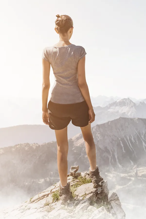 A woman triumphantly standing at the edge of a mountain peak, facing away from the camera and looking out over a vast mountain range after receiving successful Hyaluronic Acid Injections for Knee Pain by ProCare Wellness Institute in Virginia Beach.