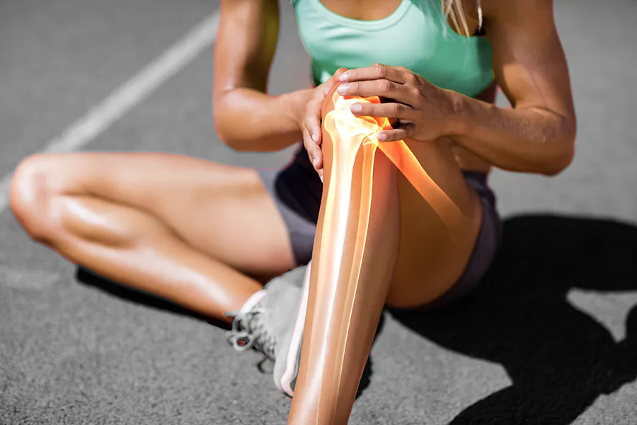 A female runner sits on the track and holds her knee in pain. Schedule treatment for MCL tears from ProCare Wellness Institute in Virginia Beach.