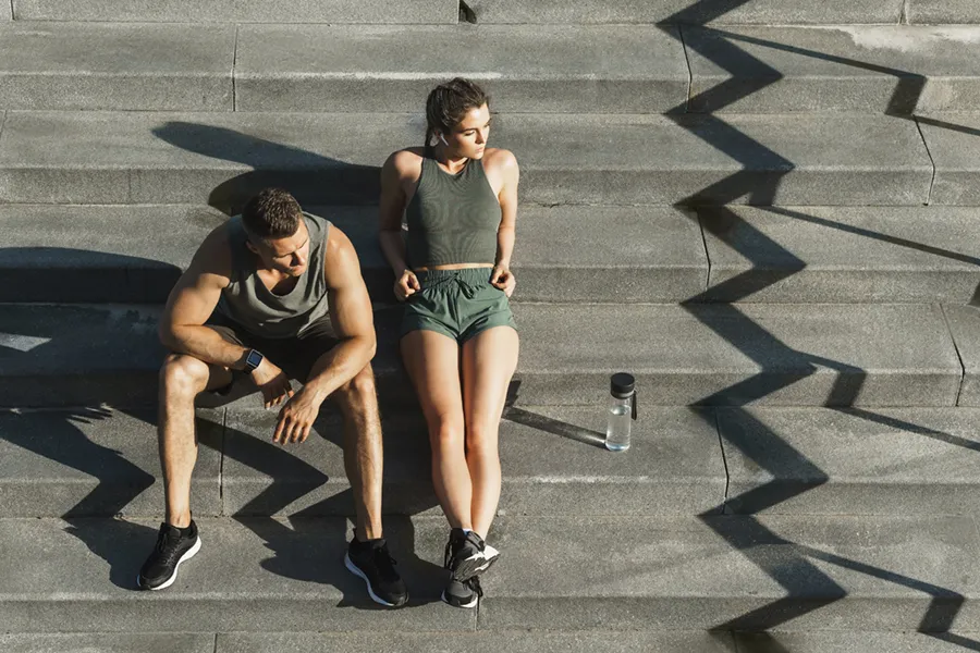 A couple in gray and green track clothes resting after a workout on stone steps, happy with their weight loss plans from ProCare Wellness Institute in Virginia Beach.