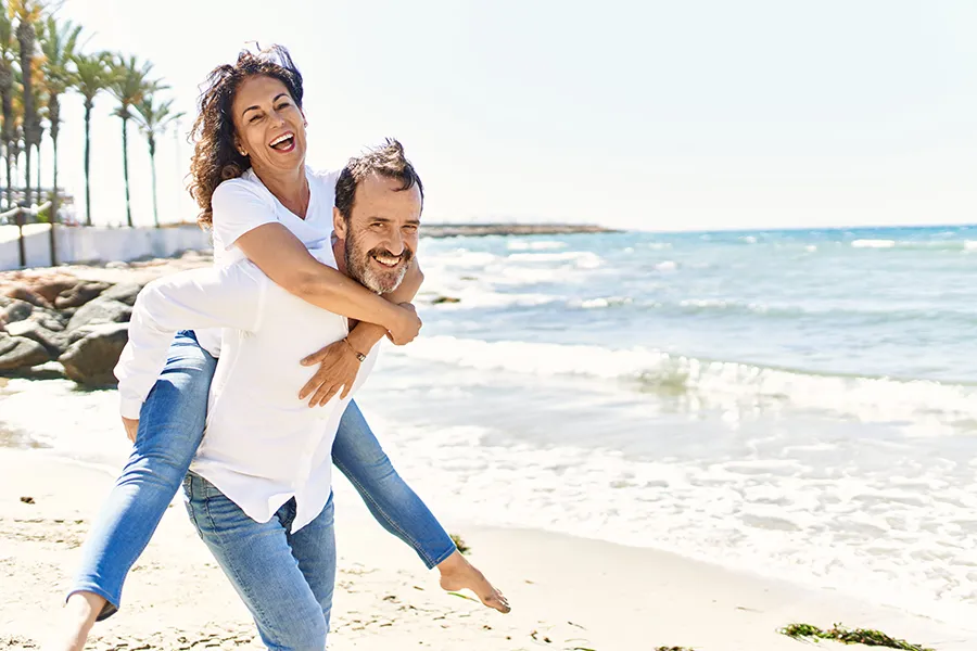 A woman piggybacks on her husband as the middle-aged couple have fun at the beach. Get NAD Therapy from ProCare Wellness Institute in Virginia Beach.