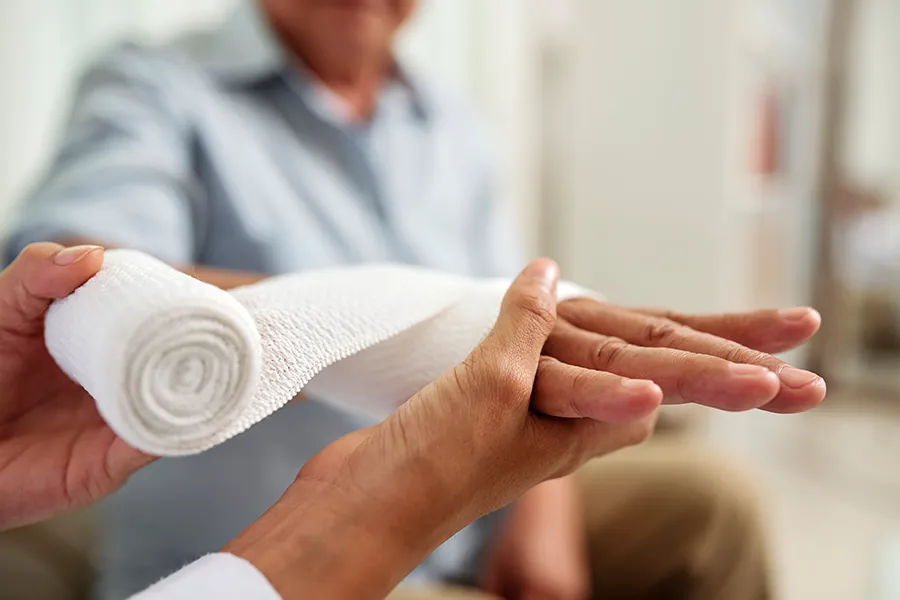 Close-up view of a healthcare professional wrapping a white bandage around a patient's wrist. ProCare Wellness Institute provides expert Non-Healing Wound Treatment in Virginia Beach.