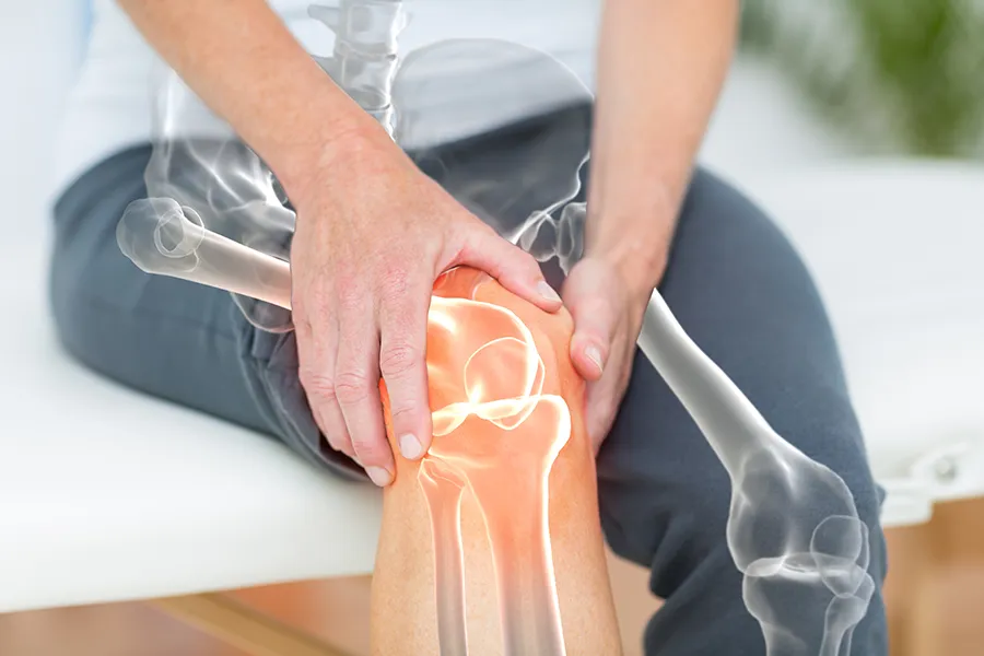A 3D illustration of the skeleton over the body of a woman who holds her knee in pain, where the area is highlighted. Schedule osteoarthritis treatment from ProCare Wellness Institute in Virginia Beach.