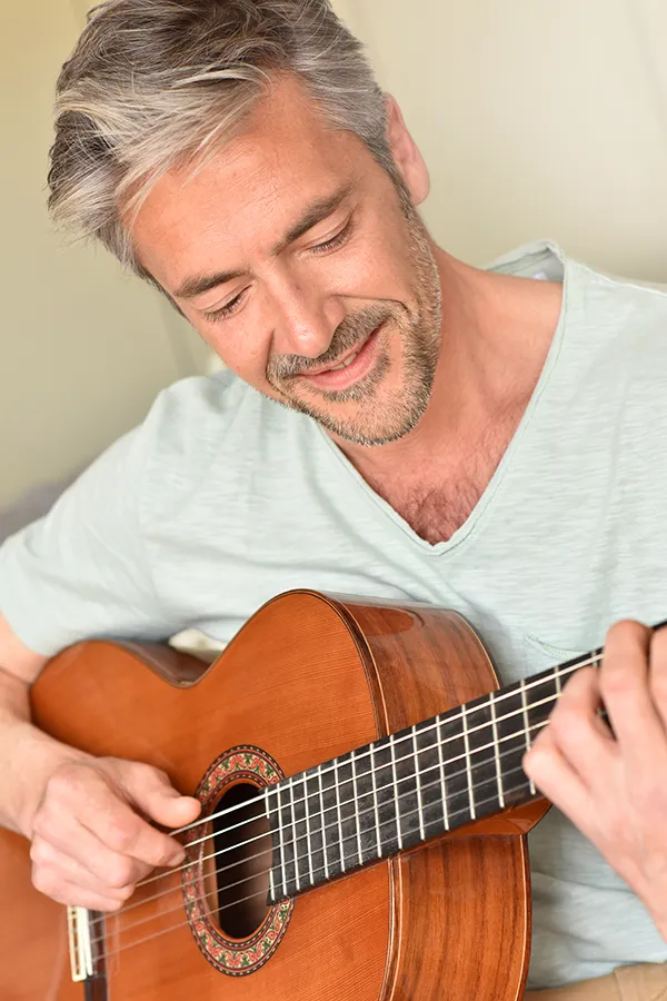 A middle-aged man happily plays guitar. Get osteoarthritis treatment from ProCare Wellness Institute in Virginia Beach.