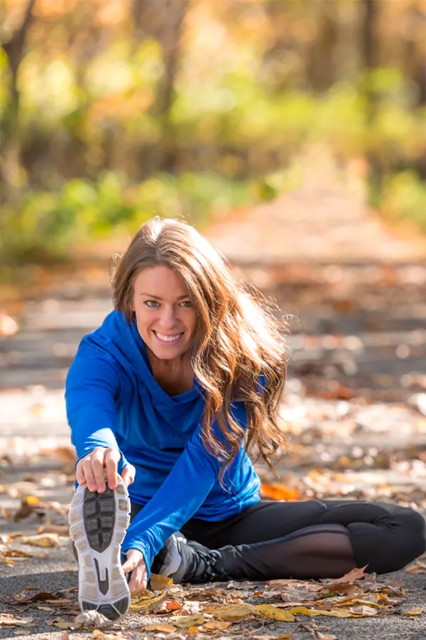 A woman in blue warm ups stretching and preparing for a run on an outdoor trail. Get Platelet Rich Plasma (PRP) treatment for sports and orthopedics from ProCare Wellness Institute in Virginia Beach.