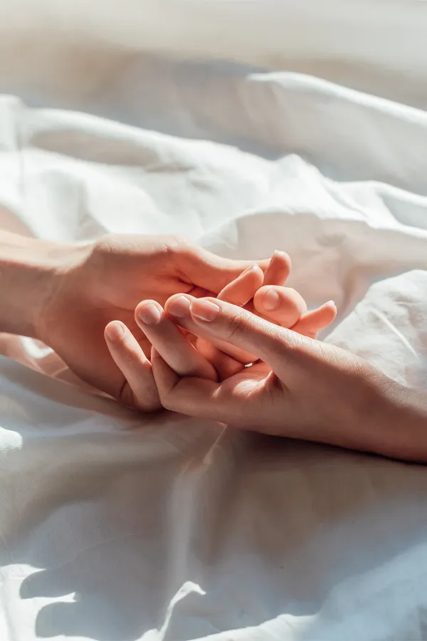 A close up of a man and woman's hands lightly clasping on a bedsheet, representing successful PT141 sexual wellness treatment for women from ProCare Wellness Institute in Virginia Beach.