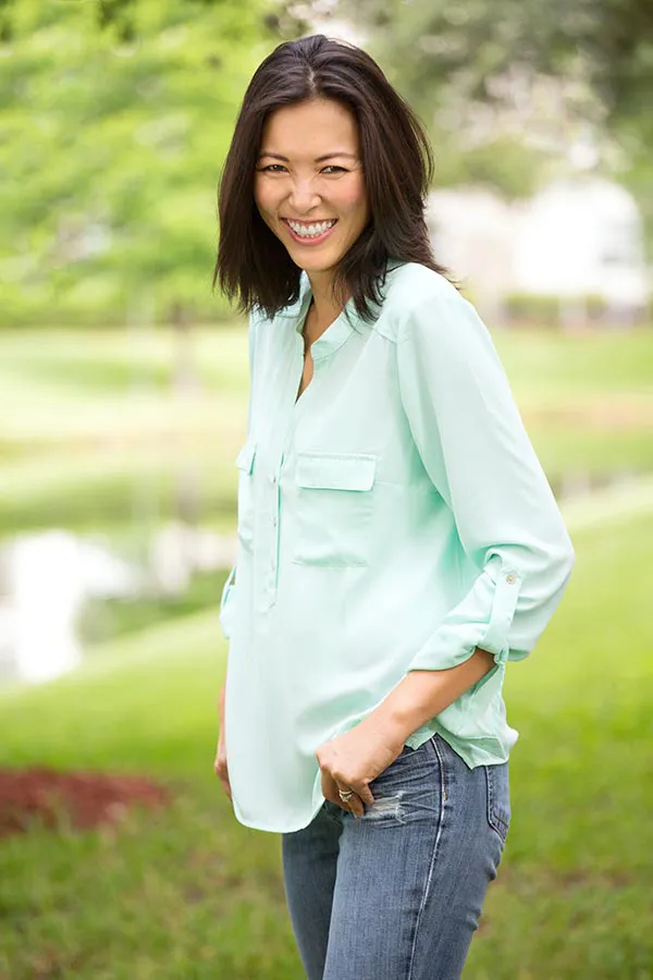 A middle-aged brunette woman in a light green button-up shirt stands outside smiling, happy with her perimenopause treatment from ProCare Wellness Institute in Virginia Beach.