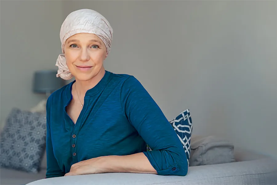 A woman wearing a headscarf, suggesting she may have undergone chemotherapy. She has a gentle smile and appears composed as she leans on a sofa in her home after successful Post-Chemotherapy Neuropathy treatment by ProCare Wellness Institute in Virginia Beach.