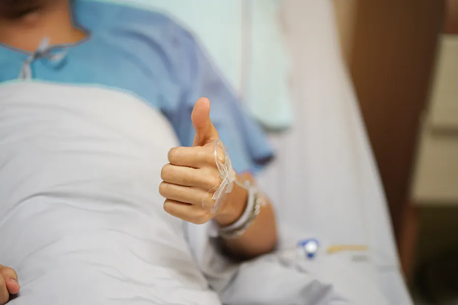 A patient gives a thumbs up while recovering in bed after surgery. Get regenerative medicine treatment for post-surgical recovery from ProCare Wellness Institute in Virginia Beach.