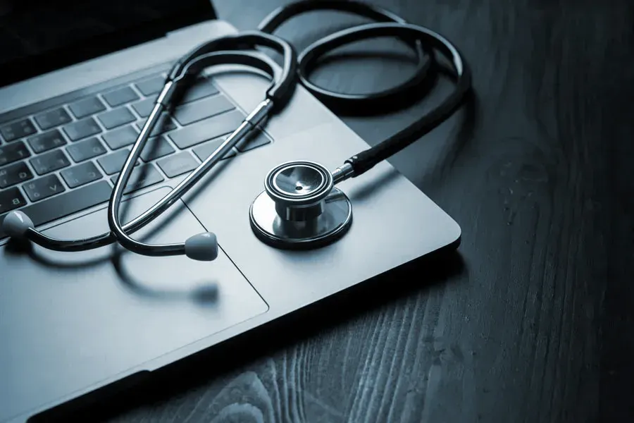 An open laptop with a stethoscope lying on it on a wooden table, symbolizing telemedicine care from ProCare Wellness Institute in Virginia Beach.