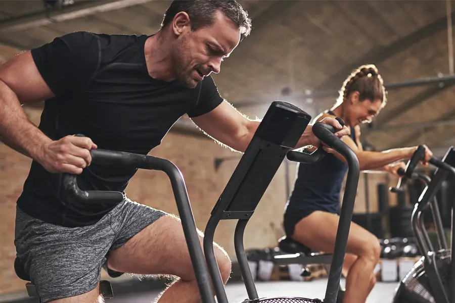 A couple in a brick gym work as hard as they can on exercise bikes, inspired by successful Tirzepatide treatment from ProCare Wellness Institute in Virginia Beach.