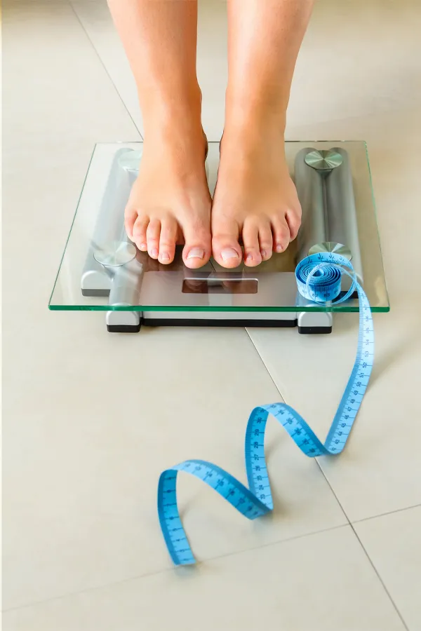 Close-up of a woman's feet standing on a scale, with measuring tape by her toes, getting treatment for weight loss resistance from ProCare Wellness Institute in Virginia Beach.